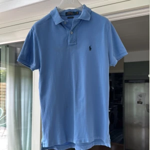 Blå pikétröja Polo Ralph Lauren - Snygg ljusblå pikétröja från Polo Ralph Lauren i modellen Custom Slim Fit. Klassisk krage, korta ärmar och broderad logga på bröstet. Tillverkad i mjuk bomull som är skön mot huden. Perfekt för en clean och stilren look.