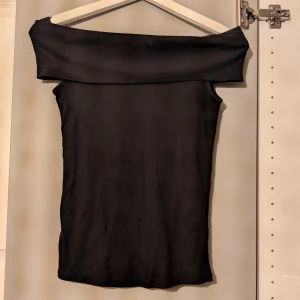 Svart offshoulder topp - Snygg svart offshoulder topp med bred kant över axlarna. Toppens tighta passform framhäver siluetten och den är perfekt att styla med höga jeans eller kjol. Enkel och stilren design som ger en cool vibe.
