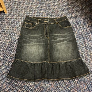 Svart jeanskjol med volang  - Snygg svart/grå jeanskjol från Cellbes i storlek 38. Kjolen har klassiska fickor fram och markerade sömmar och en bred volang längst ner. Tillverkad i stretchig denim av 98% bomull och 2% elastan för skön passform. 🩷