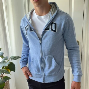 Polo full zip  - Ljusblå zip up med Polo märke. Väldigt bra skick. Sitter väldigt bra. Modellen är 178, 74 kg. Xl i barn Strlk = M/S i herr