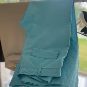 Turkosa byxor  - Snygga turkosa byxor med stora fickor fram. Byxorna har bälteshällor och stängs med knapp och dragkedja. Materialet är svalt och lätt samtidigt som det är väldigt fint på utsidan. (Oanvända. Står också strl 42 på insidan men det är mindre)