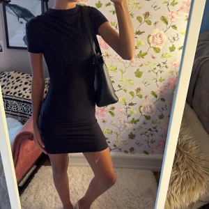 Svart klänning  - Säljer en svart, tight kortklänning med rund hals och korta ärmar. Klänningen har en enkel och stilren design som sitter figurnära och är perfekt för dig som gillar minimalistisk stil. Materialet känns mjukt och stretchigt mot kroppen.