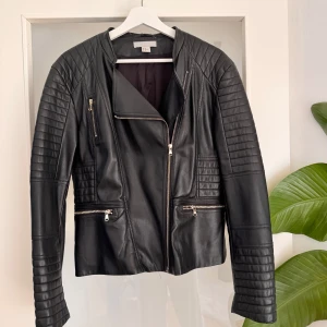 Svart skinnjacka med dragkedjor - Snygg svart skinnjacka från H&M med coola quiltade detaljer på axlar och ärmar. Jackan har flera dragkedjor framtill och en rak, lite kortare passform. 