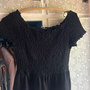 Svart smockad klänning Gina Tricot - Svart kortklänning från Gina Tricot med smockad överdel och korta ärmar. Klänningen har en rundad halsringning och är tillverkad i mjukt bomullstyg. Perfekt för dig som gillar en enkel men trendig look.