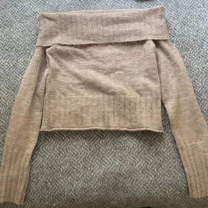 Beige offshoulder stickad tröja Urban Outfitters - Superfin beige stickad tröja från Urban Outfitters med offshoulder-design och ribbade detaljer vid ärmslut och nederkant. Perfekt för dig som gillar en chill men ändå snygg look. Mjuk och skön, passar till allt från jeans till kjol.