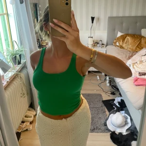 Grön ribbad croppad linnetopp - Snygg grön croppad linnetopp med breda axelband och rundad halsringning. Toppen är ribbad och sitter tight mot kroppen, perfekt för en fräsch och trendig look. Enkel att matcha med både kjol och jeans för en cool vardagsstil.