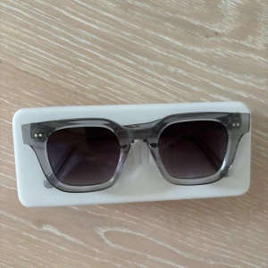 Chimi grå 04 glasögon - Snygga solglasögon från CHIMI med transparent grå båge och fyrkantig form. Glasen är mörka och ger en cool vibe. Perfekta för att lyfta din stil på sommaren. Säljes med originalfodral.