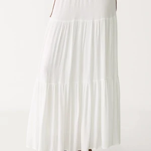 Vit långkjol - Superfin vit långkjol med volanger och flowig känsla. Kjolen har en luftig och lätt design med resår i midjan, perfekt för varma dagar. Enkel att styla med crop tops eller stickade tröjor.