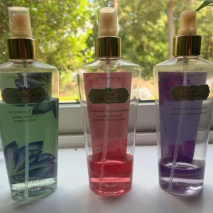 Victoria's Secret Fragrance Mist trio - Tre snygga body mists från Victoria's Secret: True Escape (grön med blå blommor), Pure Daydream (rosa med blommotiv) och Wild Nectarine (lila med lila/rosa blommor). Alla i genomskinliga plastflaskor med guldfärgade spraykorkar, 250 ml vardera.