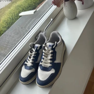 Axel Arigato sneakers blå/vit strl 41 - Snygga sneakers från Axel Arigato i vitt och mörkblått skinn. Klassisk låg modell med rund tå, perforerade detaljer och vita snören. Perfekta för dig som gillar stilrena och sportiga vibes. Handgjorda i Portugal. Nypris 2800kr. Jättebra skick och inga tydliga defekter, förutom att de har blivit lite ”creasade” vilket de blir efter bara en eller två användningar, skriv om ni har frågor!🥰