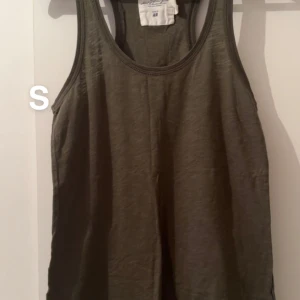 Olivgrön linnetopp från H&M - Enkel och stilren olivgrön linnetopp från H&M. Modellen är ärmlös med klassisk rund halsringning och rak passform. Perfekt att matcha med jeans eller shorts för en avslappnad look.🌸Fint använt skick. Storlek s