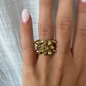 Edblad Peak Ring Gold - En efterfrågad favorit från Edblad🥰En statementring med en modern tolkning av punkiga nitar.  Ringen har en bred design med flera små konformade nitar i tre rader, vilket ger en edgy och modern känsla. Perfekt för dig som vill sticka ut med dina accessoarer😄Detaljer:         Nickelsäkert och vattentålig🙌🏼(Nypris 399kr)