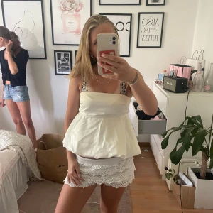 Vit bandeau tubtopp med volang - Supersöt vit bandeau tubtopp med volangig, utsvängd nederdel. Toppen är axelbandslös och har en luftig, flowy passform som ger en trendig och somrig vibe. Perfekt att styla med kjol eller jeansshorts för en fräsch look.