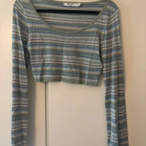 Randig croppad topp från NA-KD - Superfin croppad långärmad topp från NA-KD i tunnt material. Toppen har ett randigt mönster i blått, grönt, grått och vitt med rundad halsringning. Perfekt för dig som gillar en chill och trendig stil.