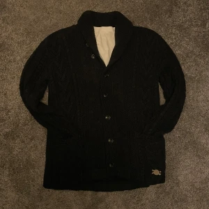 Svart cardigan från Ralph lauren - Mysig svart stickad cardigan från Ralph lauren. Koftan har två fickor och en liten broderad detalj nertill. 