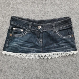  jeanskjol med spetskant - Supersöt mörkblå jeanskjol med vit spetskant nertill. Kjolen har klassiska jeansfickor fram och bak, bälteshällor och en liten dragkedja på ena bakfickan. Perfekt för dig som gillar denim med en söt twist! Märket miss here & there