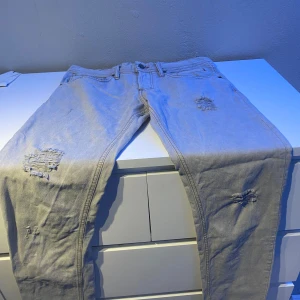 Ljusgrå ripped jeans från D&G - Snygga ljusgrå jeans från Dolce & Gabbana med slitna detaljer och regular fit. Använda en gång. Modellen är loose och har klassisk femficksdesign, raka ben och coola slitningar på låren och knäna. Perfekta för en avslappnad streetstyle-look. Inköpta för 2895kr. Lite större i midjan men passar perfekt med bälte.