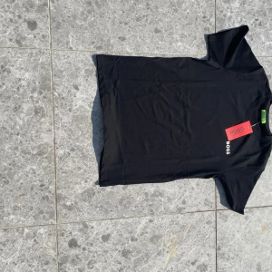 Svart t-shirt från Hugo Boss - Svart t-shirt från Hugo Boss med vit BOSS-logga på bröstet. Klassisk rund halsringning och korta ärmar. Tillverkad i mjuk bomull för en clean och stilren look. Perfekt för dig som gillar minimalistisk design och premiumkänsla.