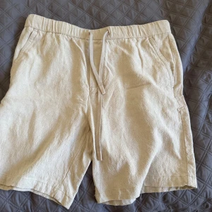 Beiga linneshorts från Zara med snörning - Snygga beiga shorts från Zara i storlek L, tillverkade i linneblandning med diskret struktur. De har elastisk midja med snörning, sidofickor och en bakficka. Perfekta för chill dagar när du vill ha en clean och avslappnad look.