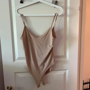 Beige linnetopp med smala axelband - Snygg beige linnetopp i bodystyle med smala axelband och djup v-ringning. Perfekt att styla med jeans eller kjol för en clean look. Mjuk och stretchig bomull som sitter skönt mot kroppen.