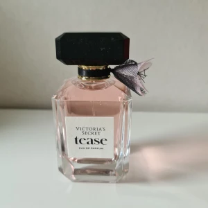 Victoria's Secret Tease Parfym 100ml - Snygg parfymflaska från Victoria's Secret, Tease Eau de Parfum, 100 ml. Flaskan är i genomskinligt glas med ljusrosa doft, svart och guldig detalj vid halsen samt en söt svart-rosa rosett i tyll. Stort svart lock med lyxig känsla. Köpt i vintras men kommer inte så mycket till användning då jag har andra favoriter. Har ej kvar förpackningen tyvärr då jag trodde denna skulle stanna föralltid. Knappt använd