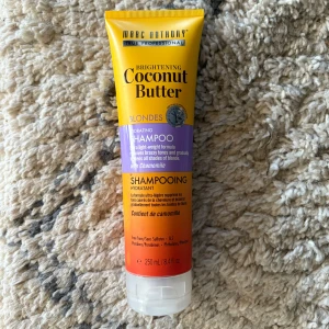 Marc Anthony Coconut Butter Shampoo - Brightening Coconut Butter Hydrating Shampoo för blont hår med kamomill. Tuben är gul, lila och orange, rymmer 250 ml och är fri från sulfater, parabener och ftalater. Ger lättviktig återfuktning och hjälper till att ta bort gula toner i blont hår.