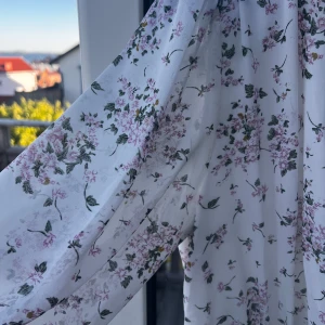 Vit blommig omlottklänning med lång ärm - Säljer en vit omlottklänning med blommigt mönster i lila och grönt. Klänningen har v-ringning, långa ärmar och rynkade detaljer framtill. Perfekt för sommarens tillfällen och har en feminin, romantisk stil.