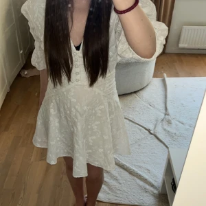 Vit blommig klänning från Adoore strl 34 - Supersöt vit klänning från Adoore med blommigt broderat mönster och djup v-ringning.🌺 Dragkedja på ryggen. Klänningen har puffiga ärmar. Perfekt till sommaren, konfirmation, student eller vad man vill💘💋☀️❤️! Säljer pågrund av att jag inte använder den längre. Dragkedjan är öppen på den bilden jag hade på mig den men kan få igen den men behöva någon som hjälper mig. Köpte för 1500 och säljer för 800 kr. Pris, fler bilder och frågor kan diskuteras privat! 