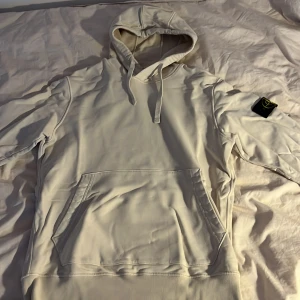 Beige hoodie från Stone Island - Säljer en stilren beige hoodie från Stone Island med klassisk patch på vänster ärm. Tröjan har huva med dragsko och en stor magficka framtill. Köpt för 3200kr. Säljer nu denna för den är för liten. Priset går att diskutera
