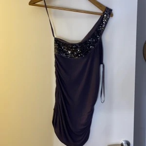 Lila paljetttröja från ONLY - Säljer en lila tröja från ONLY med paljettdetaljer längs ena axeln och halsringningen. Tröjan har oneshoulder-modell och är tillverkad i ett mjukt, syntetiskt material. Perfekt för dig som vill sticka ut på festen!