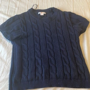 Marinblå kabelstickad kortärmad tröja från Gina Tricot - Säljer en mörkblå kabelstickad tröja från Gina Tricot med korta ärmar och rund halsringning. Tröjan har en klassisk kabelstickad design och ribbade kanter vid ärmslut och nederkant. Perfekt till vardags💗Är lite luddig men ska tvättas.