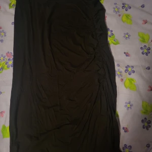 Svart tight långklänning med slits - Säljer en svart långklänning med tight passform och snygga rynkade detaljer längs sidan. Klänningen har en slits som ger extra rörelsefrihet och en stilren look. Perfekt för dig som gillar minimalistisk stil.