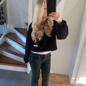 Svart teddytröja  - Mysig svart teddytröja med croppad passform och halv dragkedja framtill. Tröjan har långa ärmar och en liten vit patch nertill. 