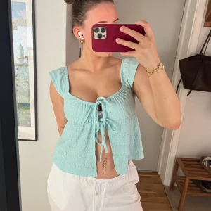 Ljusblå croppad topp från Gina Tricot - Säljer en ljusblå croppad topp från Gina Tricot med knyt framtill och volangdetaljer vid axlarna. Toppen är ärmlös och har ett hålmönster i tyget som ger en luftig känsla. Perfekt för varma dagar!