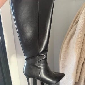 Svarta höga stövlar med klack - Säljer ett par svarta höga stövlar i skinn med spetsig tå och smal klack. Klassisk och stilren modell som passar perfekt till höst- och vinterlooken. Snygga till både kjol och byxor.