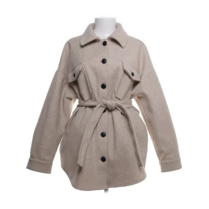 Beige jacka med bälte och svarta knappar  - Stilren beige jacka/ overshirt med svarta knappar och knytskärp i midjan. Jackan har två bröstfickor med lock och lång ärm. Perfekt för lager-på-lager och enkel att styla till olika outfits.