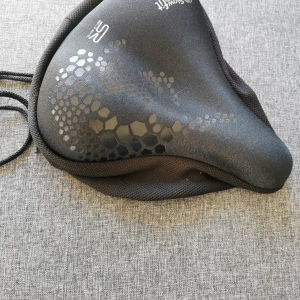 Vadderat cykelsadelöverdrag  - Överdrag till cykelsadeln för att göra den mjuk och skön och torr. Ej använd. I nyskick. Knyte bak för att få den att vara still. Passar vanliga cykelsadlar. 
