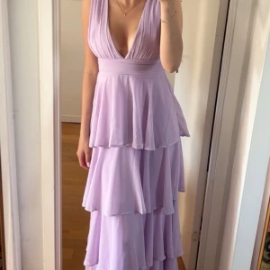 Ljuslila balklänning med volanger  - Säljer min superfina balklänning! 🌸Den är endast använd en gång och har inga problem med den, den är ljuslila med volanger ända ner till marken. Jag är 178 cm och den gick hela vägen ner till mina ballerina skor! Klänningen är i Storlek M från Lulus💕 Hoppas den kommer till användning av någon ny! 🥹💕