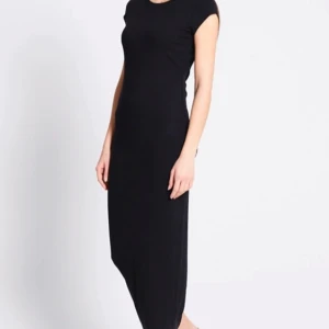Svart långklänning med kort ärm - En stilren svart långklänning med rund halsringning och korta ärmar. Klänningen har en rak passform och är tillverkad i ett mjukt, stretchigt material som sitter bekvämt mot kroppen. Perfekt för dig som gillar minimalistisk och tidlös stil.