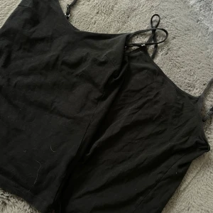 Svart linnetopp med smala axelband  - En enkel svart linnetopp från lager 157 med smala axelband och rak passform. Tillverkad i mjuk bomull med lite stretch för extra komfort. Perfekt att matcha med jeans eller kjol. 25kr för både.