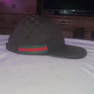 Gucci keps canvas svart - Säljer en svart keps från Gucci med klassiskt GG-mönster och grönt/rött band på sidan. Kepsen har böjd skärm och justerbart spänne bak. perfekt för dig som gillar exklusiva accessoarer. OBS… Endast seriösa och byten fungerar också 