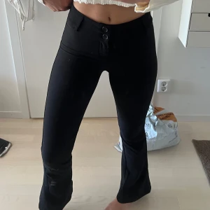 Svarta bootcut kostymbyxor med knappar - Snygga svarta kostymbyxor med bootcut passform och hög midja. Byxorna har två dekorativa knappar framtill och fickor bak. Perfekta för en stilren look och passar till många olika outfits. Från Ginatricot.
