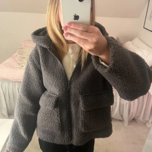 Grå teddyjacka från Zara - Snygg och cozy grå teddyjacka från Zara med huva och dragkedja. Storlek 152 men passar mig som vanligtvis brukar ha XS. Jackan har två stora fickor framtill och är perfekt för kyligare dagar. Den är tillverkad i ett fluffigt material som ger en trendig look. Använd några fåtal gånger så är i mycket bra skick. 😊
