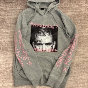 Grå hoodie med Lil Peep-tryck - Grå hoodie med stor svartvit bild av Lil Peep på bröstet och rosa texten 'EVERYBODY'S EVERYTHING' på bröstet och ärmarna. På ryggen finns tre porträtt av Lil Peep och hans namn i rosa. Mjuk insida och klassisk huva.