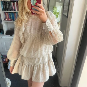 Prickig volangklänning med knappar - Supersöt kortklänning i ljusbeige med diskreta prickar och volangdetaljer. Jättefin som den är men också med ett bälte i midjan som på bild 1💕lite konstig i sömmarna på ett ställe (bild 5)