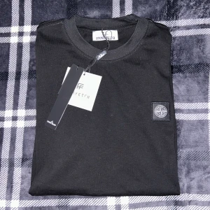 Svart t-shirt från Stone Island - Säljer en svart t-shirt från Stone Island med klassisk logotyp-patch på bröstet. T-shirten har rund halsringning och är i mjuk bomull. Perfekt för dig som gillar stilrena och exklusiva plagg.