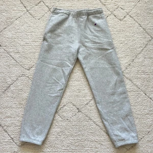 Grå mjukisbyxor från Champion - Gråa mjukisbyxor från Champion med klassisk logga broderad på vänster höft. Byxorna har resår i midjan och dragsko på insidan för extra komfort. Perfekta för chill dagar eller träning.