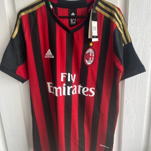 AC Milan fotbollströja Kaka 22 - Säljer en klassisk AC Milan fotbollströja från Adidas med Kaka och nummer 22 på ryggen. Tröjan är röd och svart med smala ränder, guldiga detaljer på axlarna och klubbmärke på bröstet. Kortärmad modell med Fly Emirates som sponsortryck.