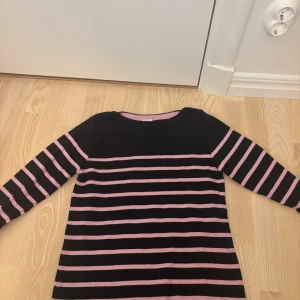 Randig tröja från Boomerang - Mysig långärmad tröja från Boomerang i svart med rosa ränder. Tröjan har knappar på axeln. I storlek S men passar xs också! Skriv för fler bilder eller andra frågor!