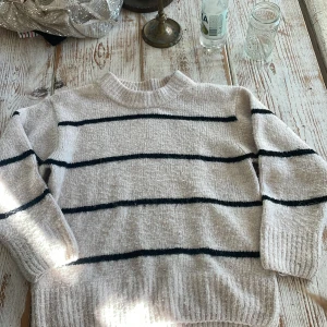 Vit stickad tröja med svarta ränder från Gina Tricot - Mysig vit stickad tröja från Gina Tricot med svarta horisontella ränder. Tröjan har rund halsringning och långa ärmar. Perfekt för kyligare dagar och enkel att matcha med jeans eller kjol.